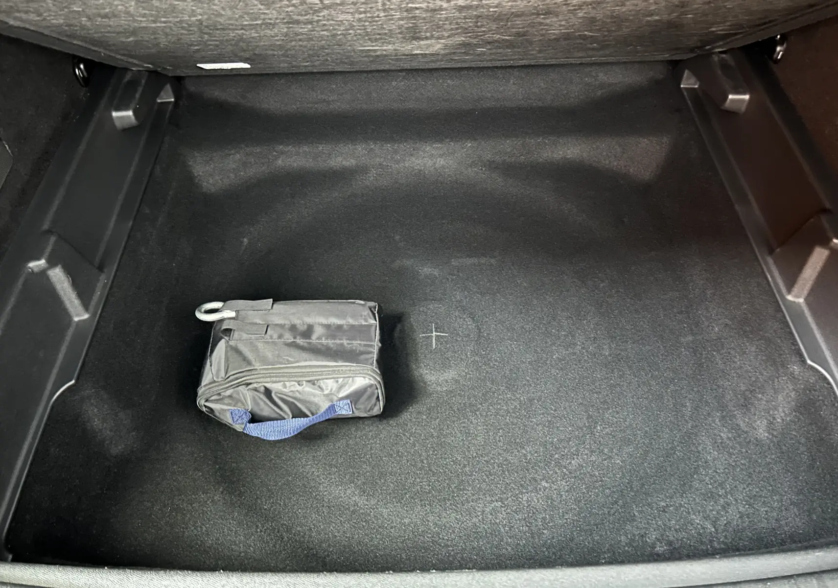 Vue plongeante sur le coffre noir du Peugeot 3008 Hybrid 2024 avec une petite trousse noire posée au centre.