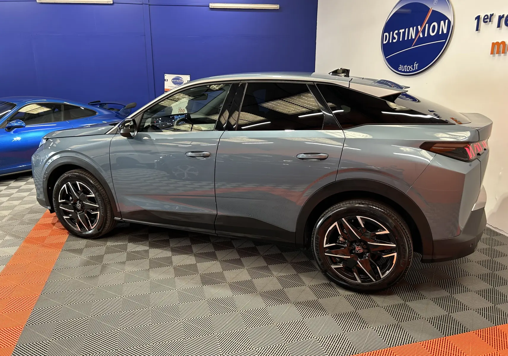 Vue de profil droit du Peugeot 3008 III Hybrid 136 bleu Ingaro avec jantes noires et toit panoramique en intérieur showroom.