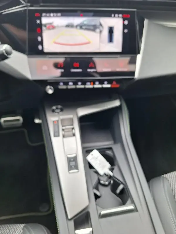 Vue intérieure centrée sur la console centrale et l'écran tactile affichant la caméra de recul du Peugeot 308 Hybrid gris.