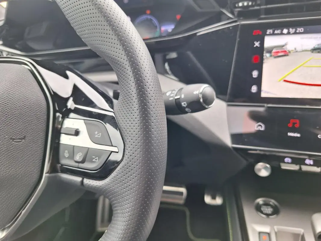 Gros plan sur le volant et l’écran tactile central de la Peugeot 308 Hybrid gris, avec affichage caméra de recul.