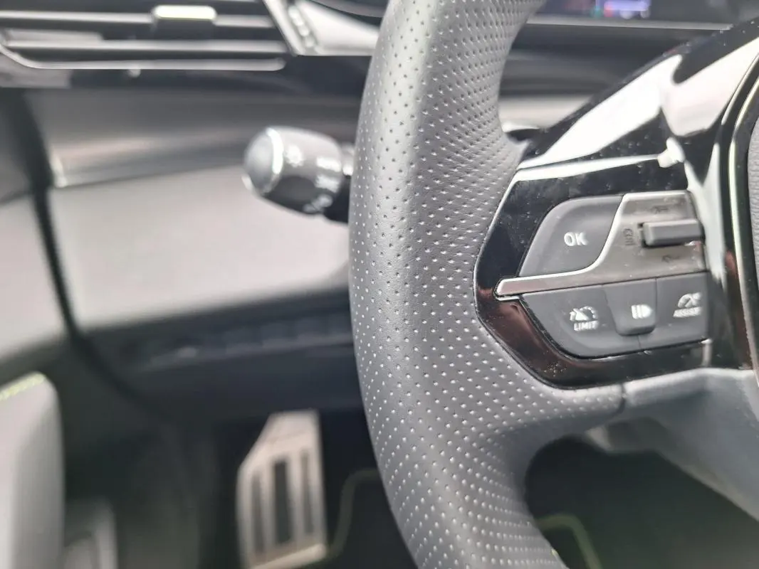 Gros plan sur le volant perforé et les commandes intégrées du Peugeot 308 Hybrid 145 e-DCS6 GT, intérieur noir.