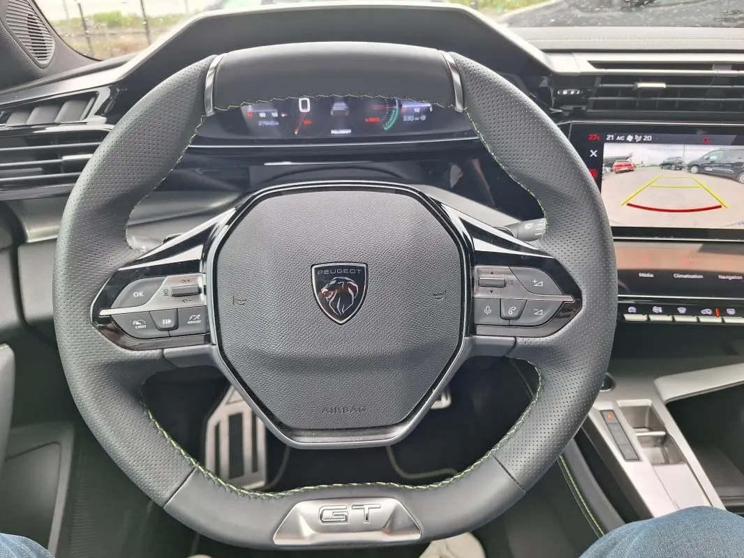 Vue rapprochée du volant gris de la Peugeot 308 Hybrid 145 e-DCS6 GT 2025 avec cockpit numérique et écran multimédia.