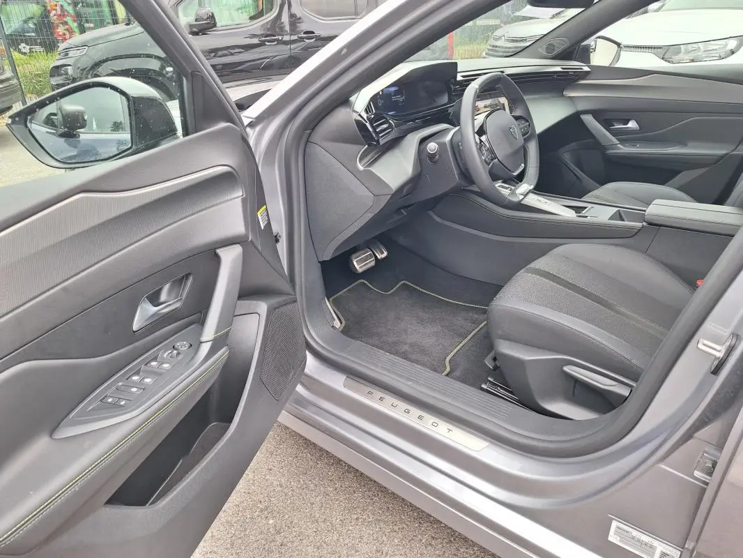 Intérieur côté conducteur d'une Peugeot 308 Hybrid gris 2025, avec porte ouverte et cockpit numérique visible.