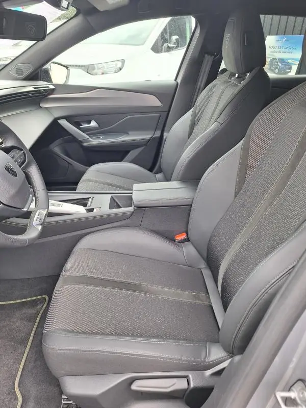 Vue intérieure côté conducteur de la Peugeot 308 Hybrid 145 e-DCS6 GT 2025, sièges gris et tableau de bord moderne.