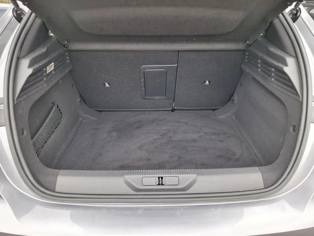 Coffre ouvert vu de l'arrière d'une Peugeot 308 Hybrid 145 gris, montrant un espace de chargement propre et spacieux.