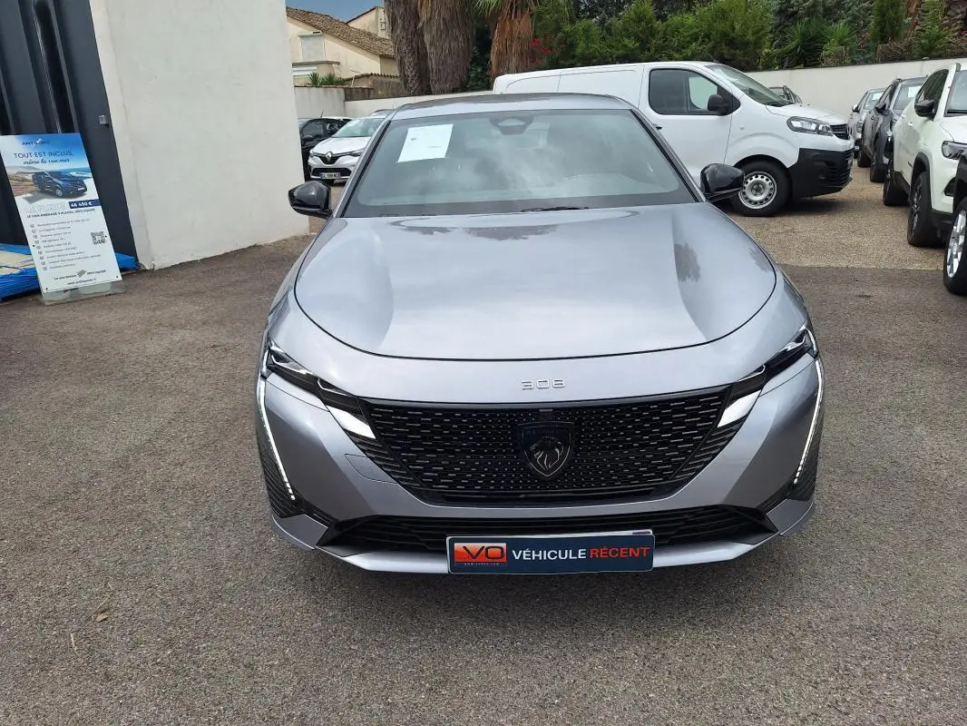 Vue avant d'une Peugeot 308 Hybrid 145 e-DCS6 GT gris métallisé avec calandre noire et feux LED verticaux.