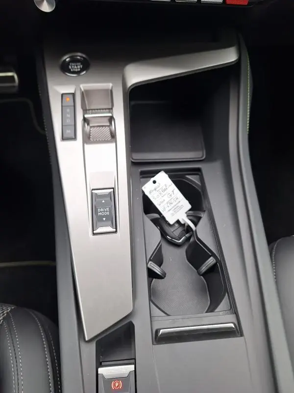 Vue rapprochée de la console centrale grise de la Peugeot 308 Hybrid 145 e-DCS6 GT avec levier de vitesses automatique et porte-gobelets.