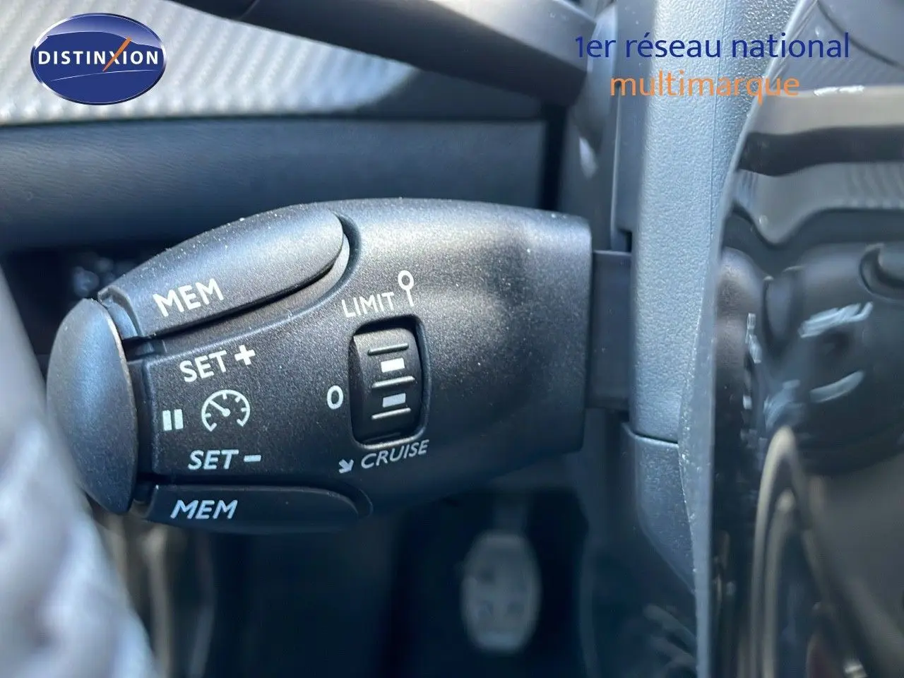 Gros plan sur la commande de régulateur de vitesse à gauche du volant dans le Peugeot 2008 rouge Elixir Metal 2025.