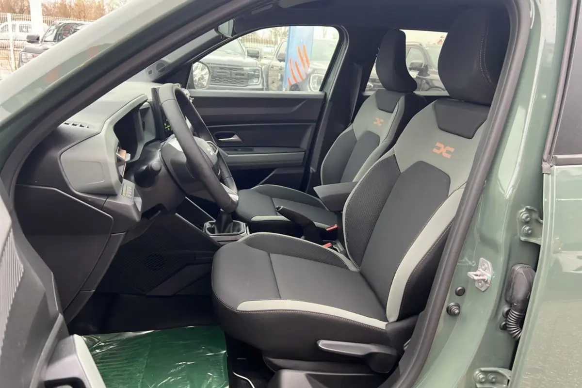 Intérieur côté conducteur du Dacia Duster 2025 kaki lichen, sièges noirs et gris avec logo orange sur appuie-tête.