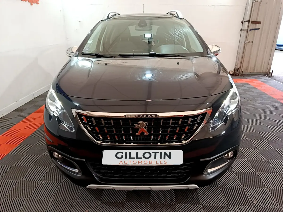 Vue avant d'un Peugeot 2008 gris foncé avec calandre chromée et phares allumés dans un garage.