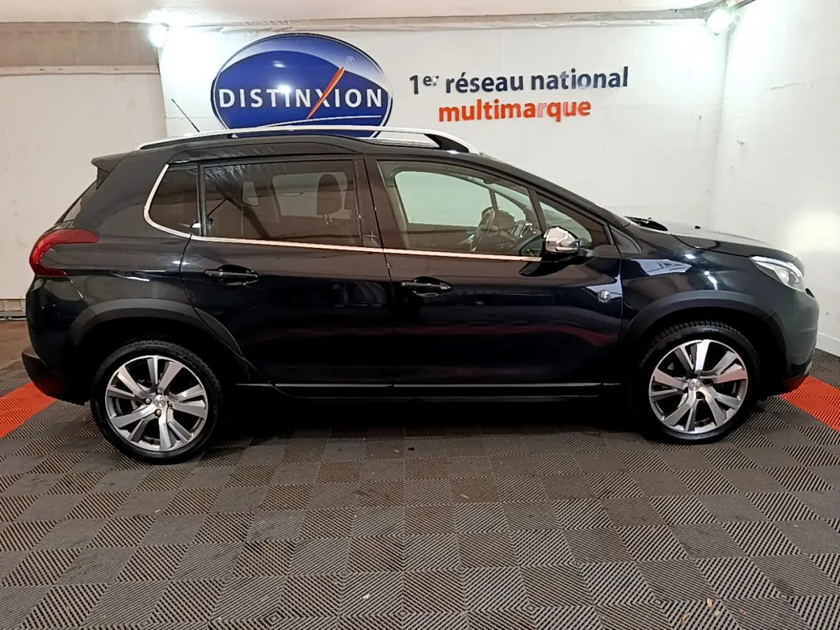 Peugeot 2008 gris foncé vue de profil côté gauche, avec jantes alliage et barres de toit chromées visibles