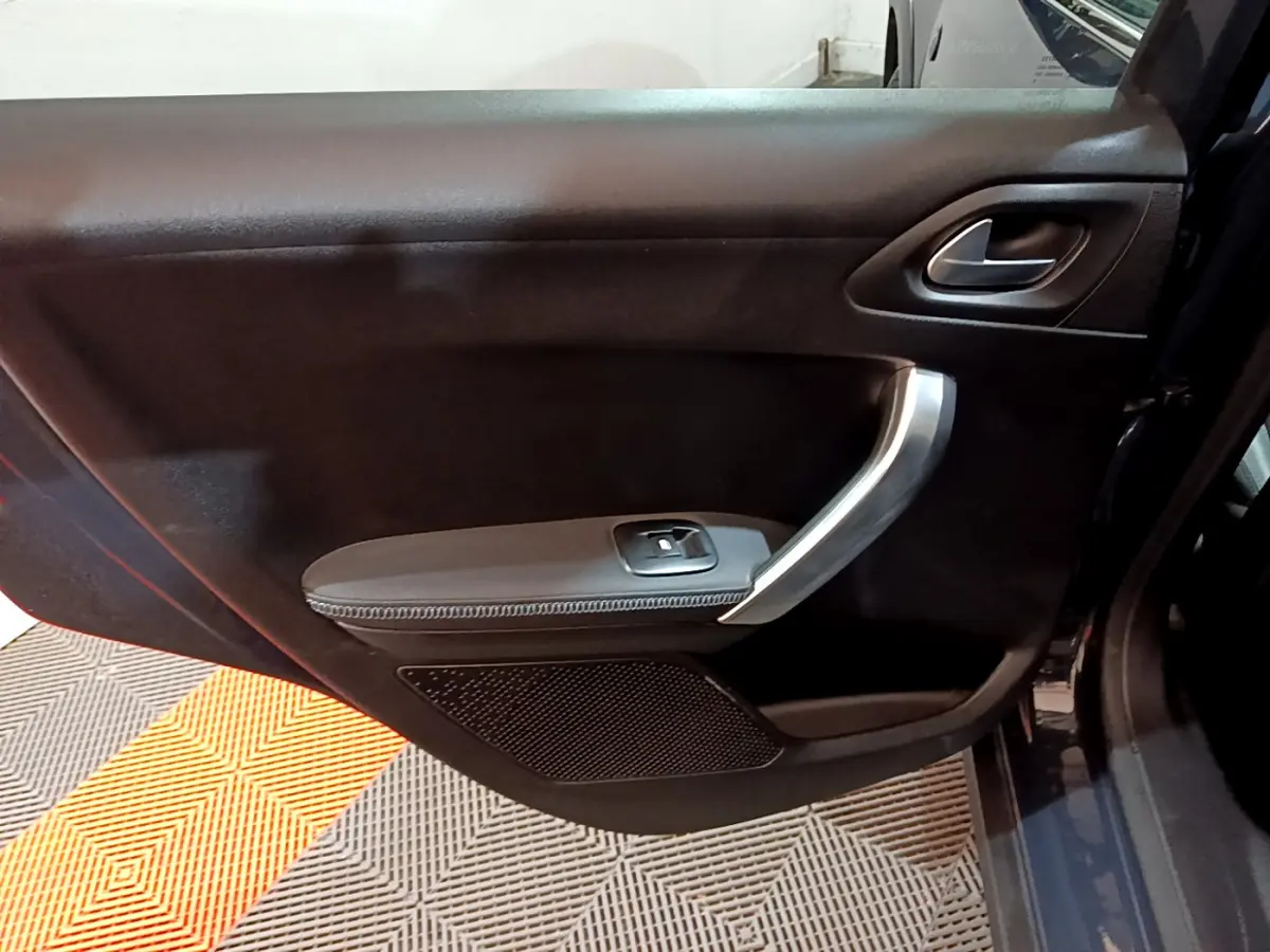 Gros plan sur la porte intérieure côté droit d'un Peugeot 2008 gris foncé, avec poignée argentée et commande de vitre.