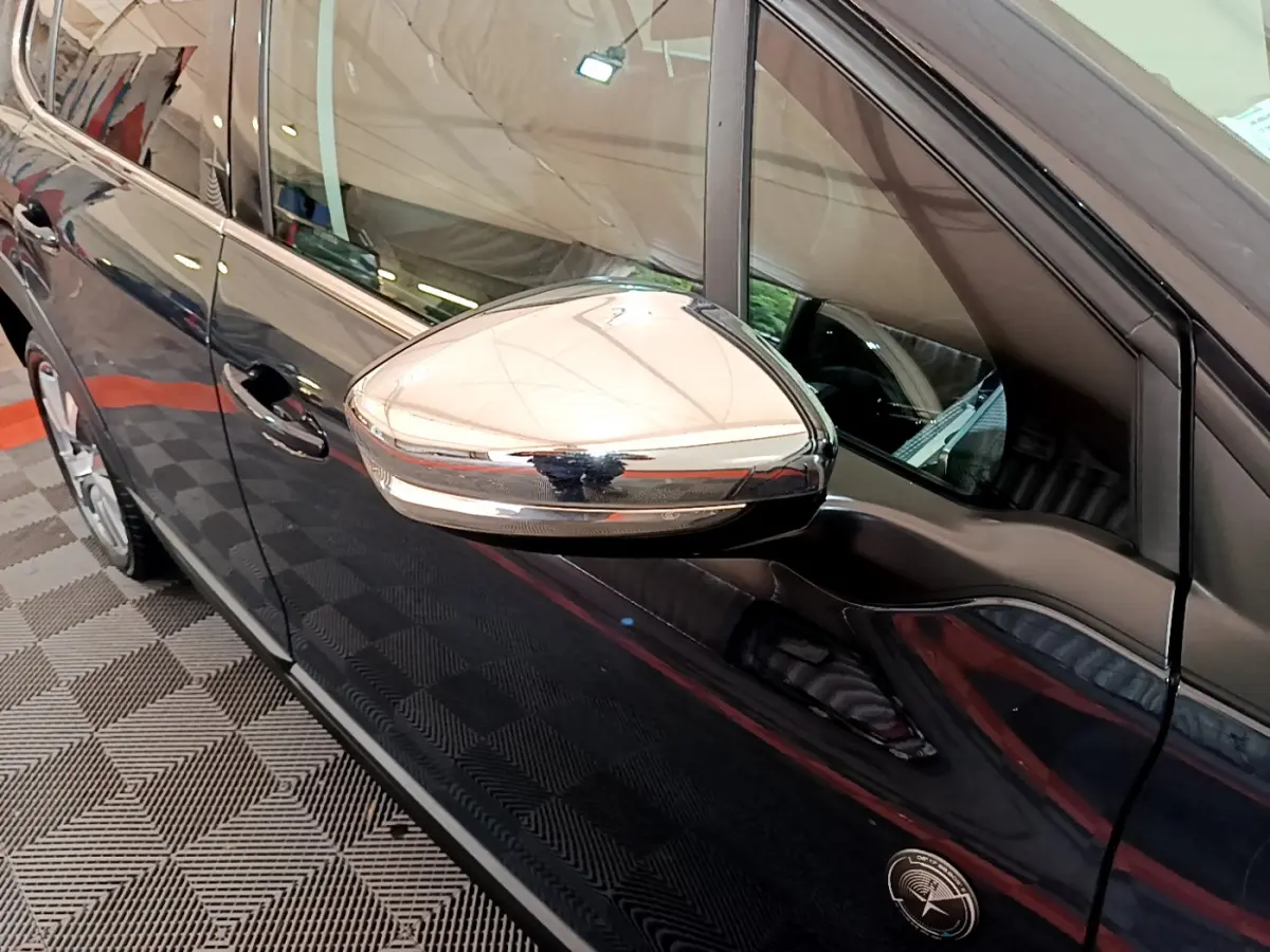 Rétroviseur chromé en gros plan sur le côté gauche d'un Peugeot 2008 gris foncé, vue latérale intérieure.