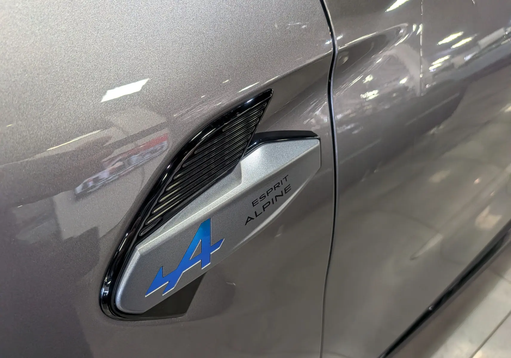 Gros plan sur l'aile avant gauche gris Cassiopé du Renault SYMBIOZ E-TECH avec logo bleu Alpine Esprit.
