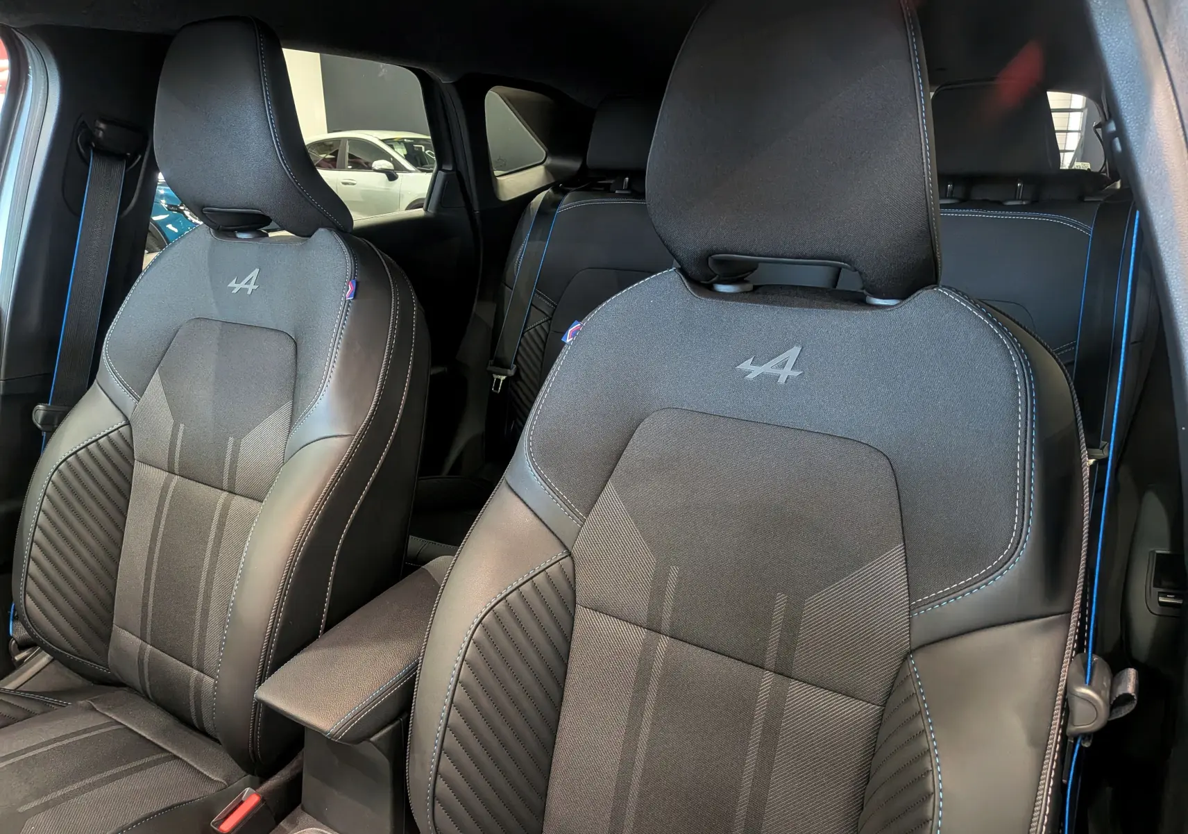 Vue intérieure rapprochée des sièges avant noirs avec surpiqûres bleues et logo Alpine sur un Renault Symbioz hybride 2026.