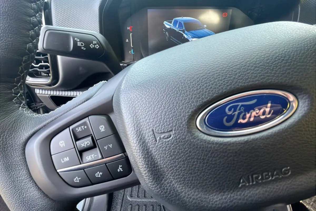 Gros plan sur le volant cuir multifonctions d’un Ford Ranger 2025 avec écran digital affichant un pick-up bleu.