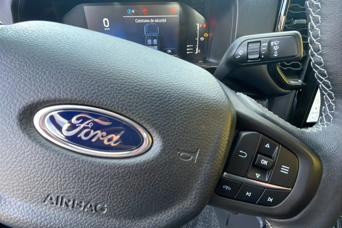 Gros plan sur le volant en cuir noir du Ford Ranger 2025 avec commandes multifonctions et tableau de bord numérique visible.