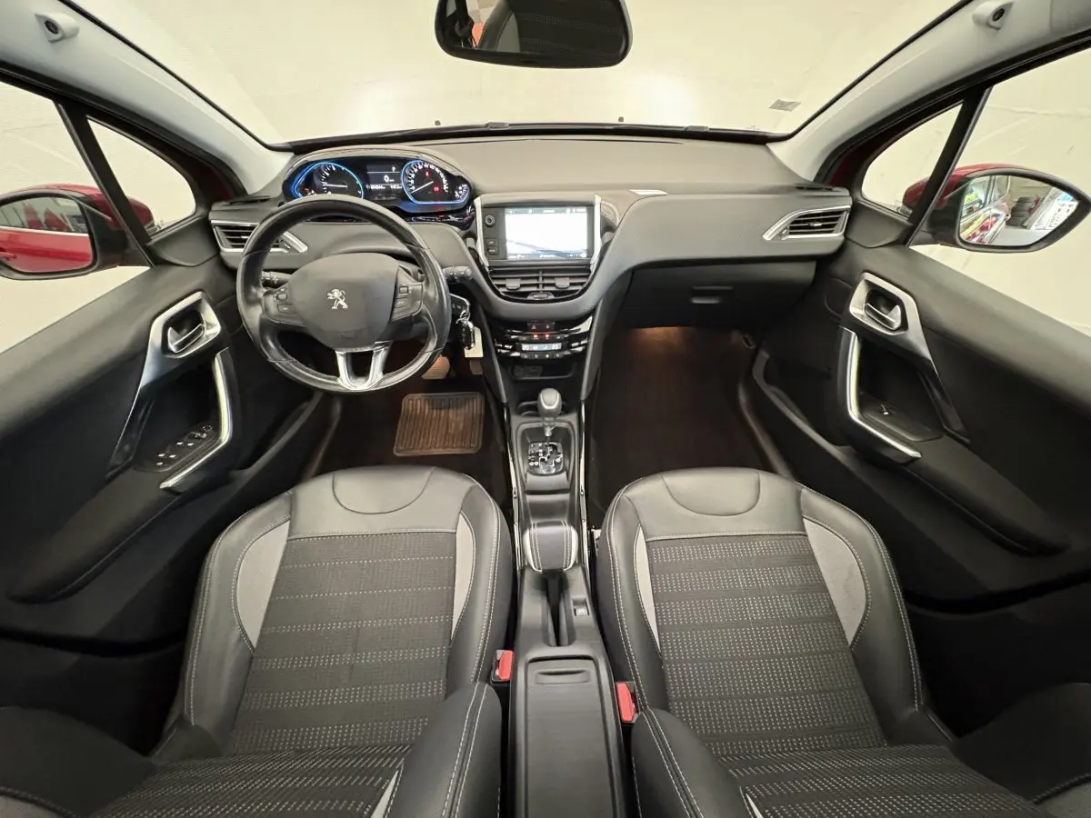 Intérieur avant de la Peugeot 2008 rouge 2019, vue centrée sur le tableau de bord et les sièges noirs en cuir.