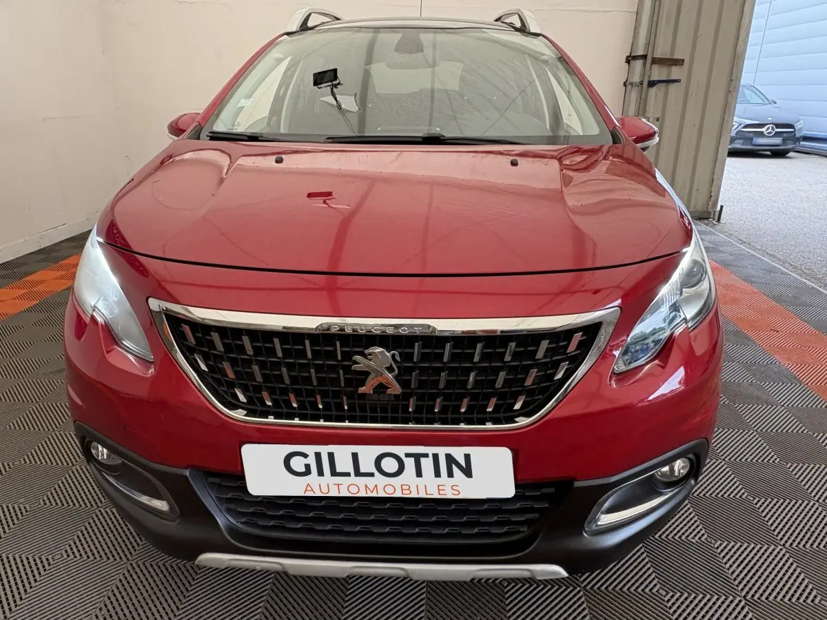 Peugeot 2008 rouge vue de face dans un garage, avec calandre chromée et phares allumés.