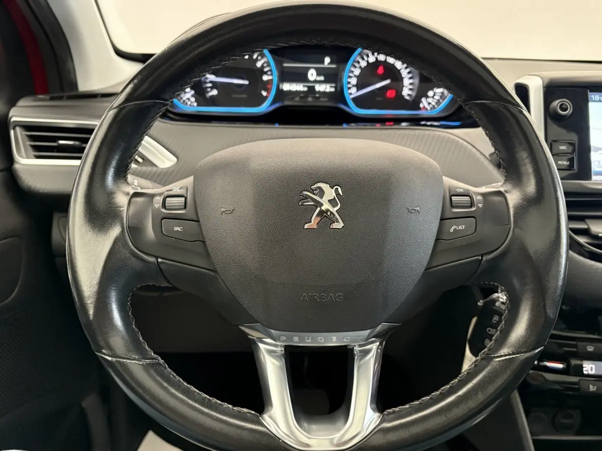 Gros plan sur le volant cuir noir du Peugeot 2008 rouge, avec tableau de bord numérique et commandes intégrées.