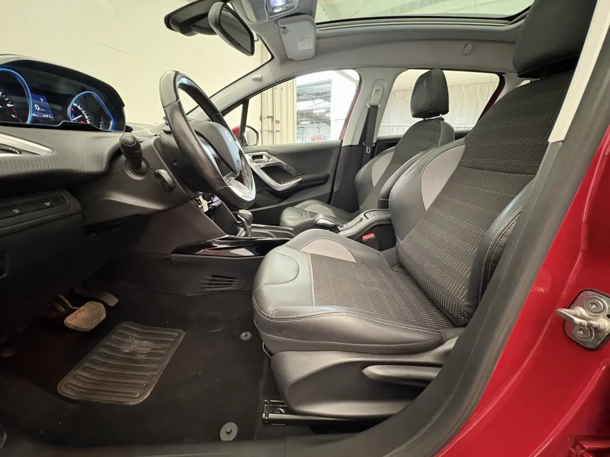 Intérieur avant droit d'une Peugeot 2008 rouge 2019, sièges en cuir noir et gris, volant multifonctions et toit panoramique visible.