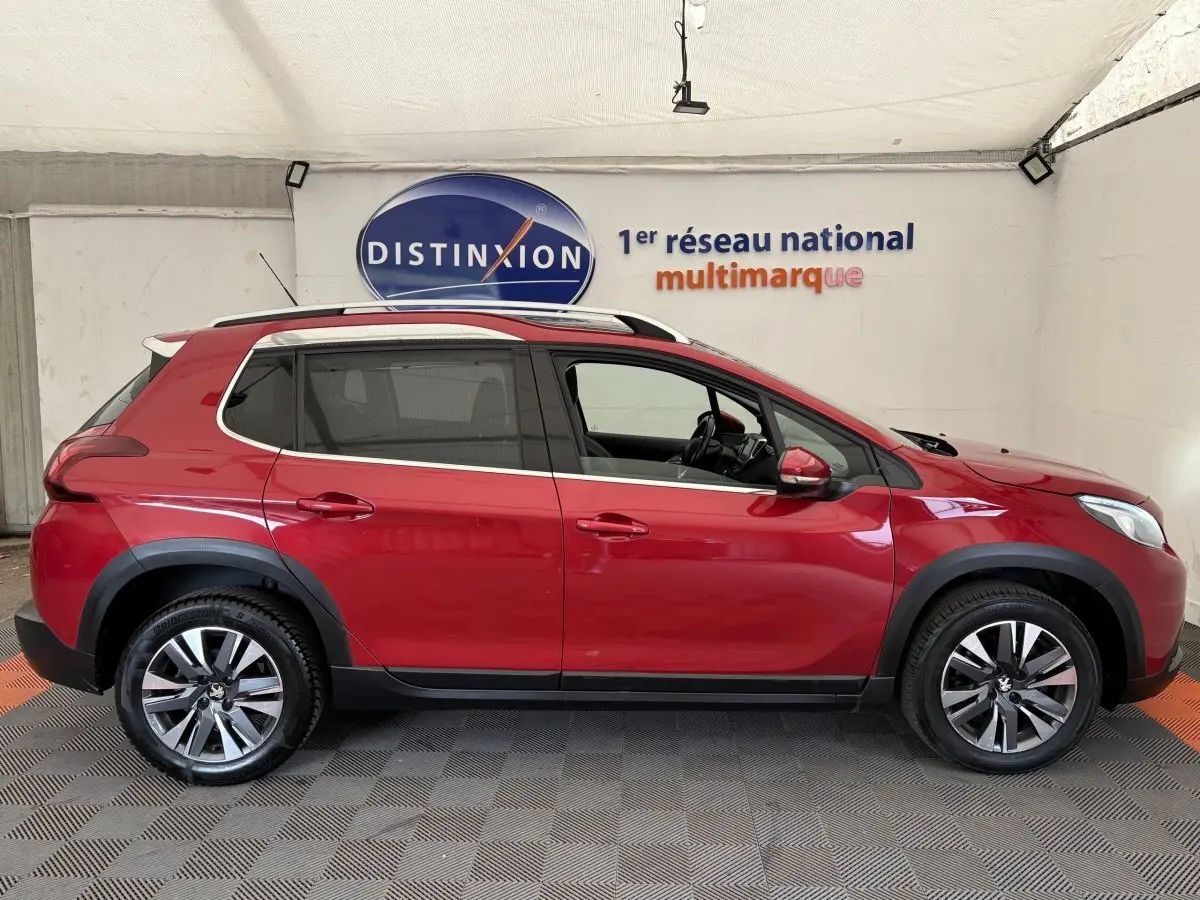 Profil côté gauche d'un Peugeot 2008 rouge 2019 avec jantes alliage et barres de toit chromées dans un showroom.