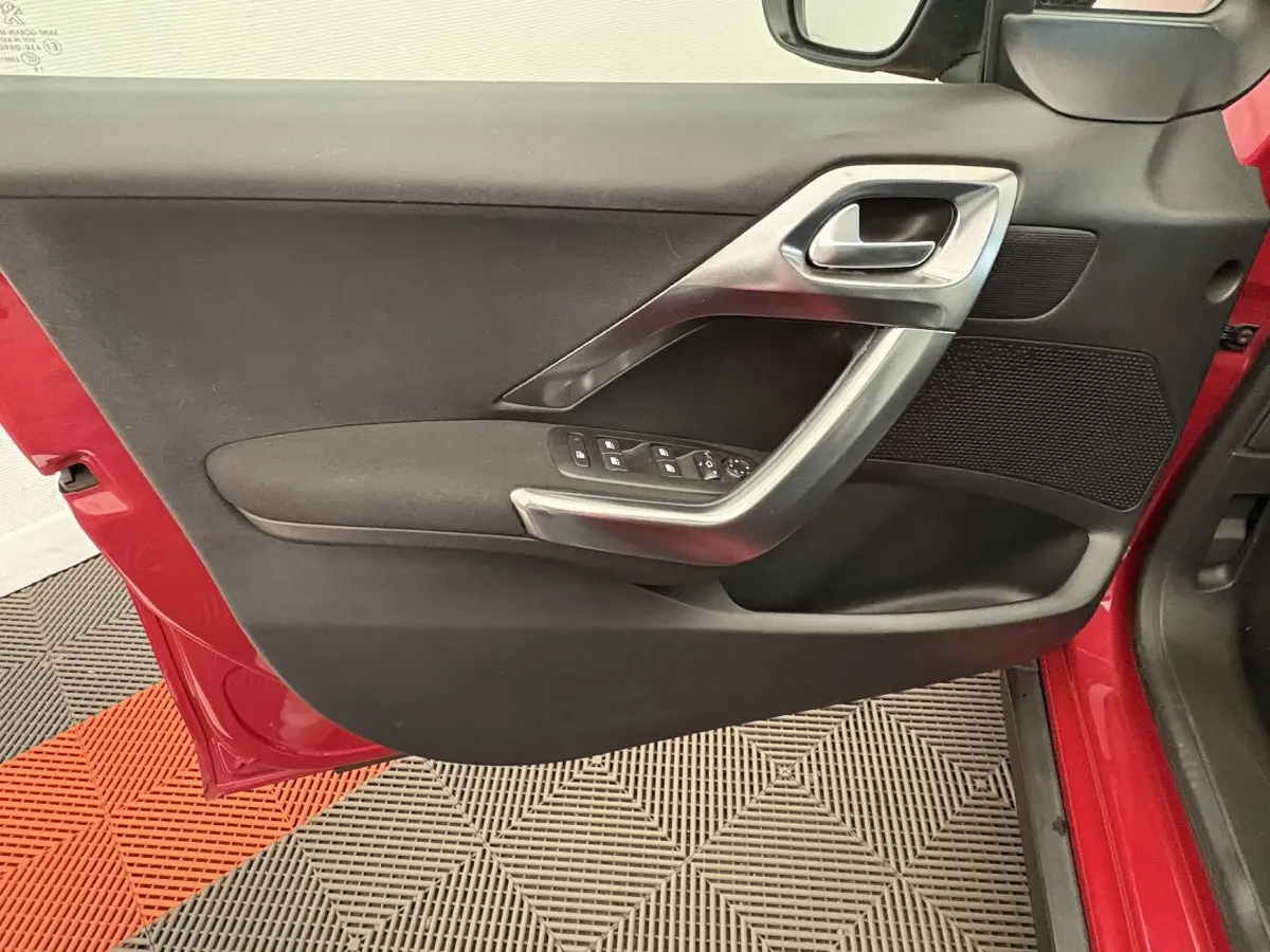 Vue rapprochée de la porte avant gauche rouge d'un Peugeot 2008 2019, avec poignée argentée et commandes de vitres.