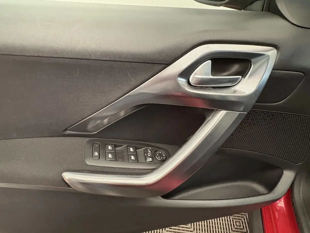 Gros plan sur la porte côté conducteur rouge d'un Peugeot 2008 2019, avec commandes des vitres et poignée argentée.