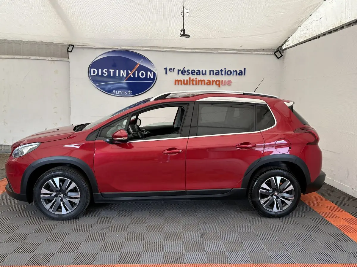 Profil droit d'un Peugeot 2008 rouge 2019 avec barres de toit chromées et jantes alliage dans un showroom.