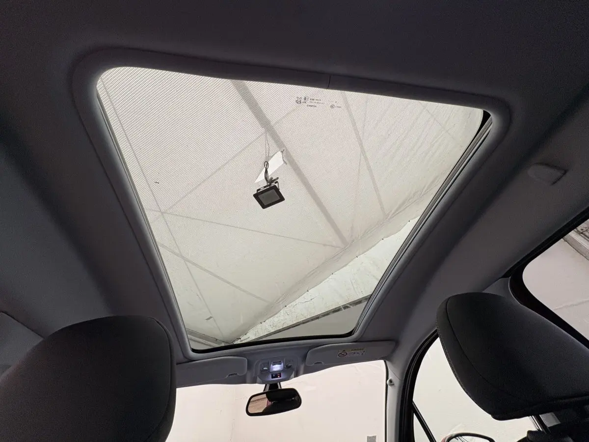 Toit panoramique ouvert vu de l'intérieur avant du Peugeot 2008 rouge, montrant les sièges avant et le rétroviseur central.