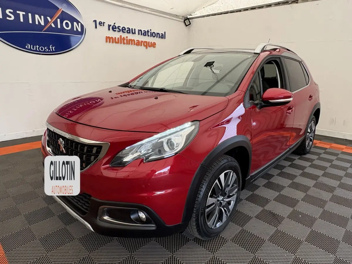 Peugeot 2008 rouge vue 3/4 avant droit, avec phares LED et barres de toit chromées en intérieur showroom.