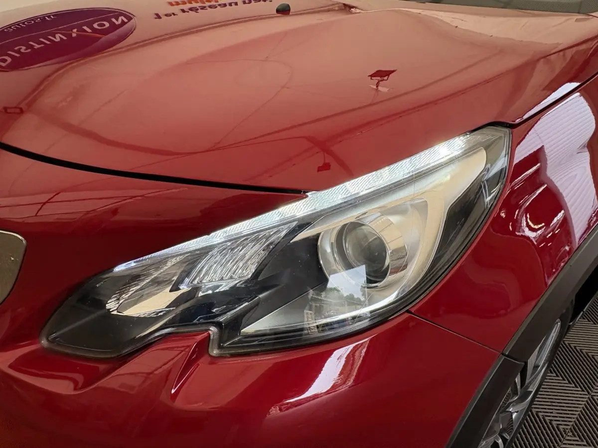 Gros plan sur le phare avant droit d'une Peugeot 2008 rouge brillant, soulignant ses lignes modernes et précises.