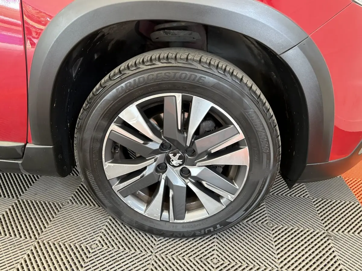 Gros plan sur la roue avant gauche d’un Peugeot 2008 rouge avec jante alliage et pneu Bridgestone.