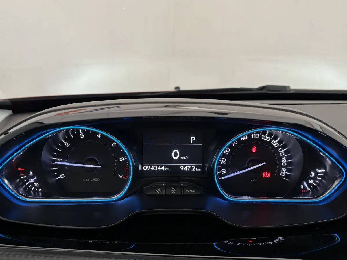 Tableau de bord numérique bleu de Peugeot 2008 rouge, affichant compteur et vitesse à 0 km/h en vue frontale.