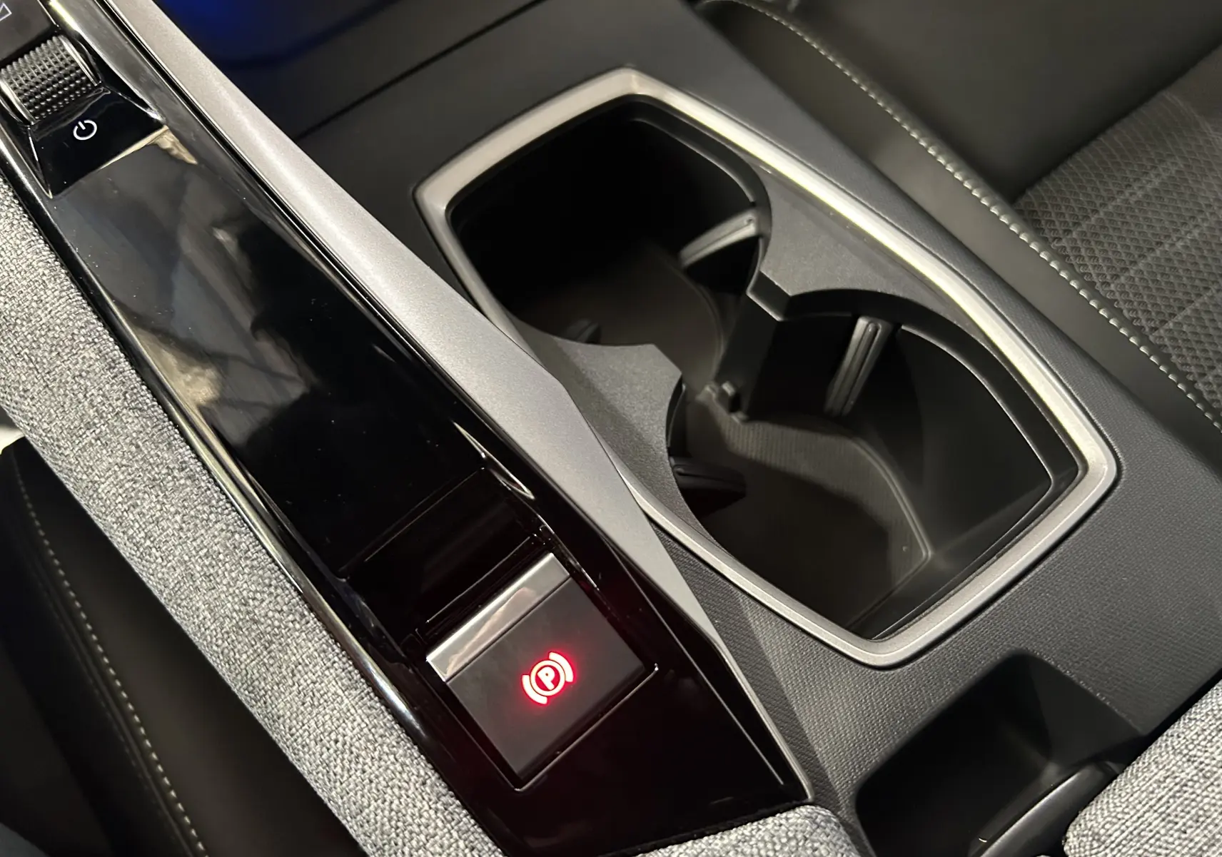 Gros plan sur la console centrale intérieure du Peugeot 3008 gris Artense, avec porte-gobelets et bouton frein à main électrique éclairé.