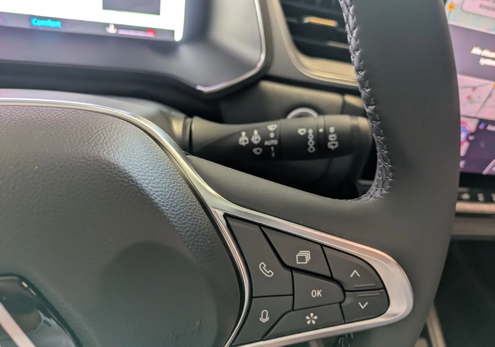 Gros plan sur les commandes multifonctions du volant en tissu du Renault Captur rouge Désir 2025, avec tableau de bord numérique en arrière-plan.