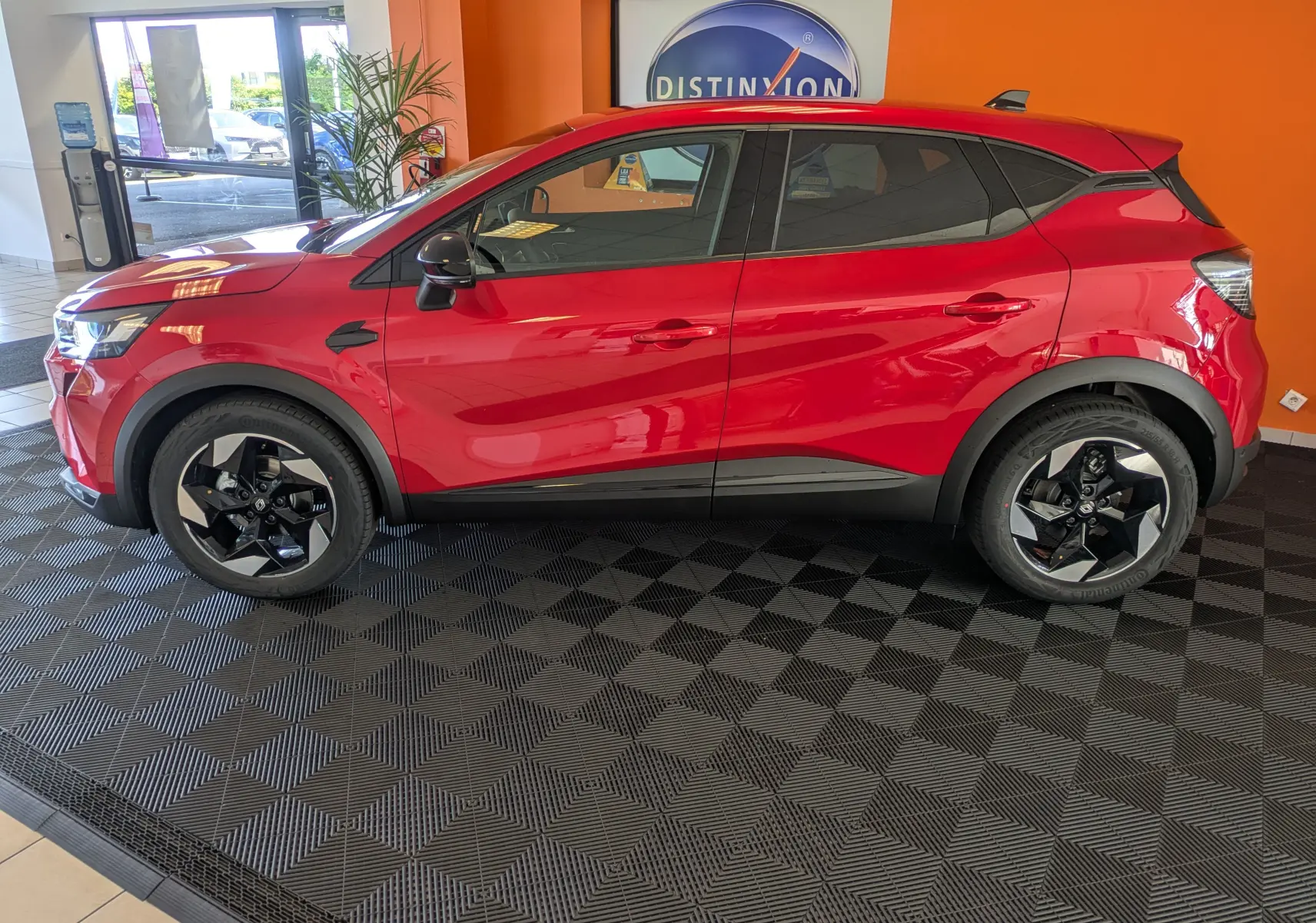 Profil côté gauche du Renault Captur 2025 rouge désir avec jantes alliage 18'' Pasadena et toit noir en showroom.