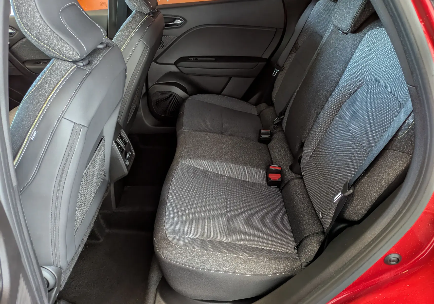 Vue intérieure côté droit sur la banquette arrière grise du Renault Captur rouge Désir 2025 avec sellerie tissu.