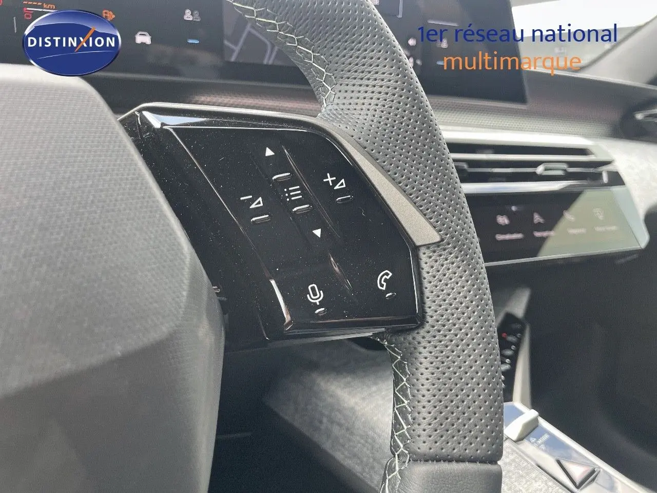 Gros plan sur les commandes gauche du volant perforé du Peugeot 5008 Hybrid 2025, tableau de bord en arrière-plan.