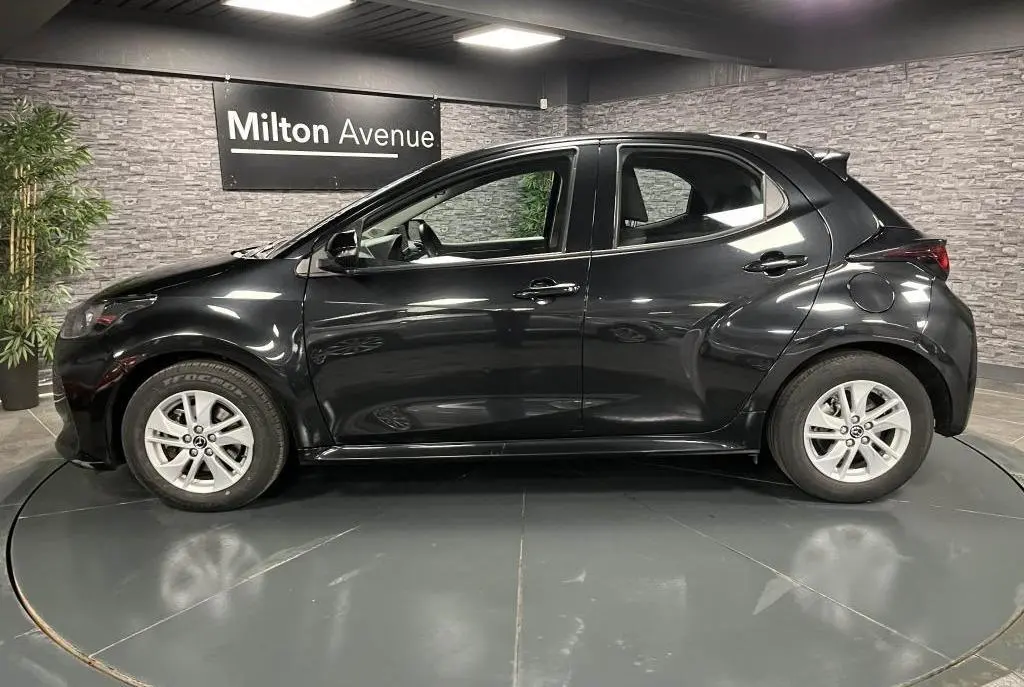 Vue de profil côté gauche d'une Mazda2 noire 2023 avec jantes alliage 15 pouces dans un showroom intérieur.