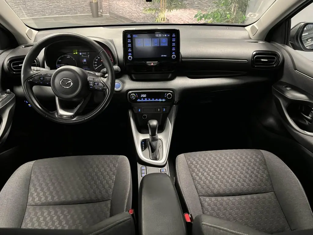 Intérieur noir de la Mazda2 2023, vue frontale sur le tableau de bord avec écran tactile et volant cuir multifonction.