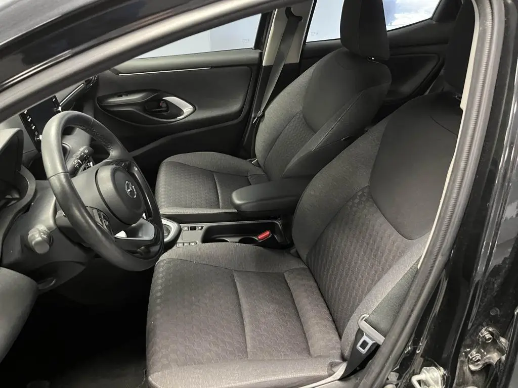 Intérieur avant droit de la Mazda2 noire 2023, sièges tissu noir et accoudoir central avec rangement visible.