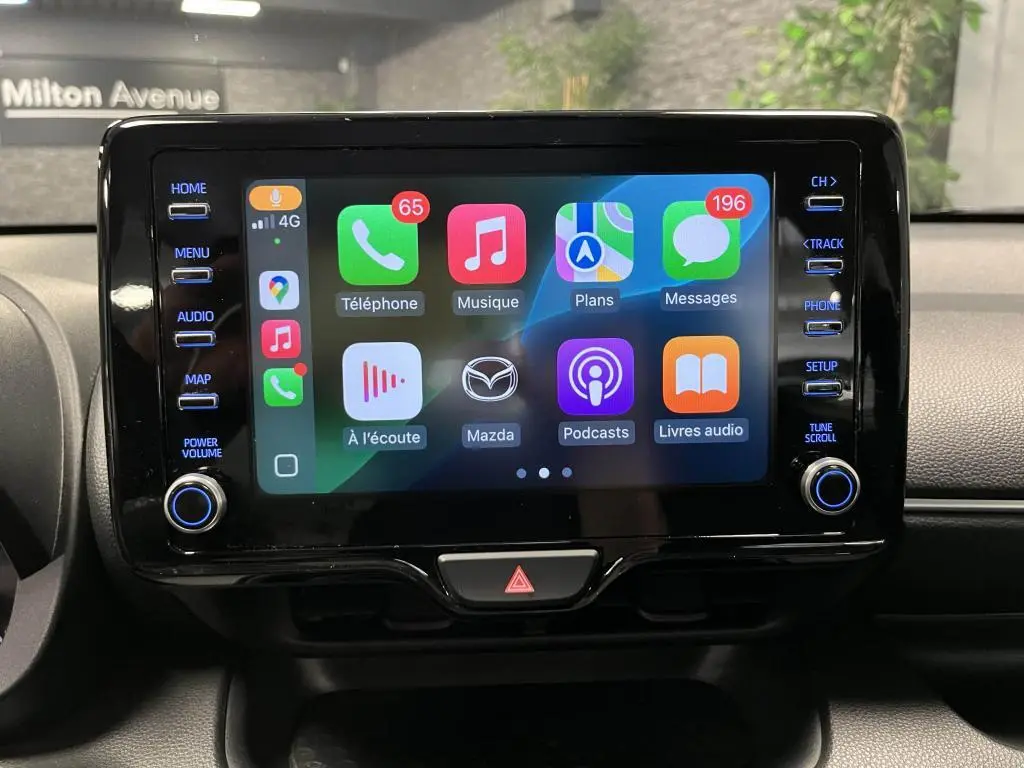 Écran tactile central de la Mazda2 2023 affichant Apple CarPlay avec commandes latérales et bouton de volume.