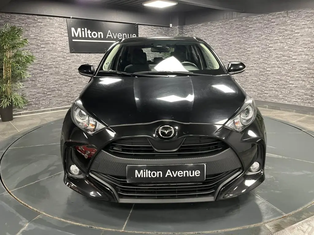 Vue frontale d'une Mazda2 noire 2023 avec calandre noire et projecteurs halogènes dans un showroom.