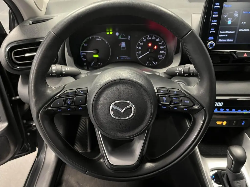 Vue frontale du volant en cuir noir de la Mazda2 2023 avec commandes intégrées et tableau de bord digital lumineux.