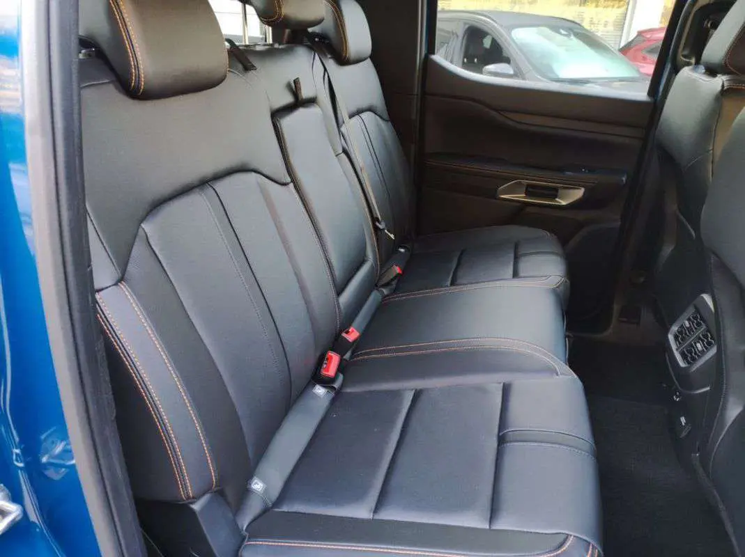 Vue intérieure côté gauche des sièges arrière en cuir noir avec surpiqûres orange du Ford Ranger 2025 bleu lightning Wildtrak Plus.
