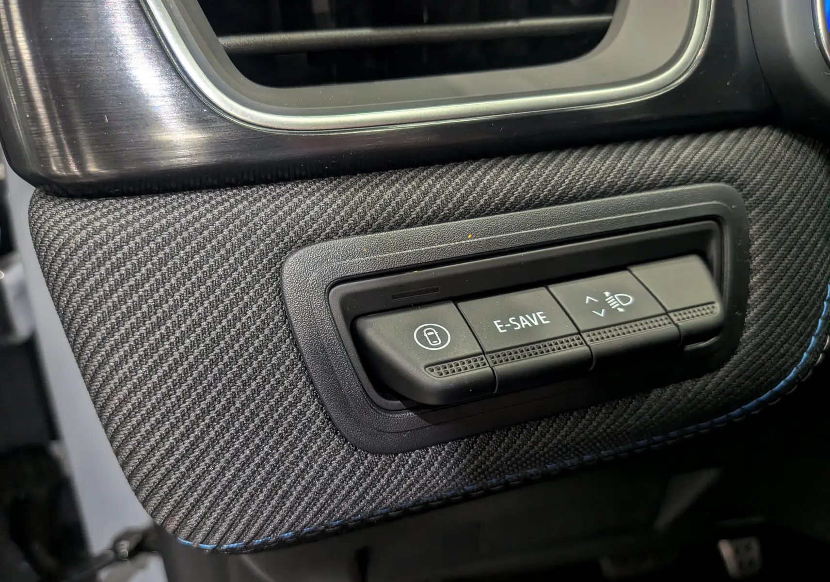 Gros plan sur les commandes E-SAVE et réglage des phares sur la planche de bord en tissu gris du Renault Symbioz E-TECH.