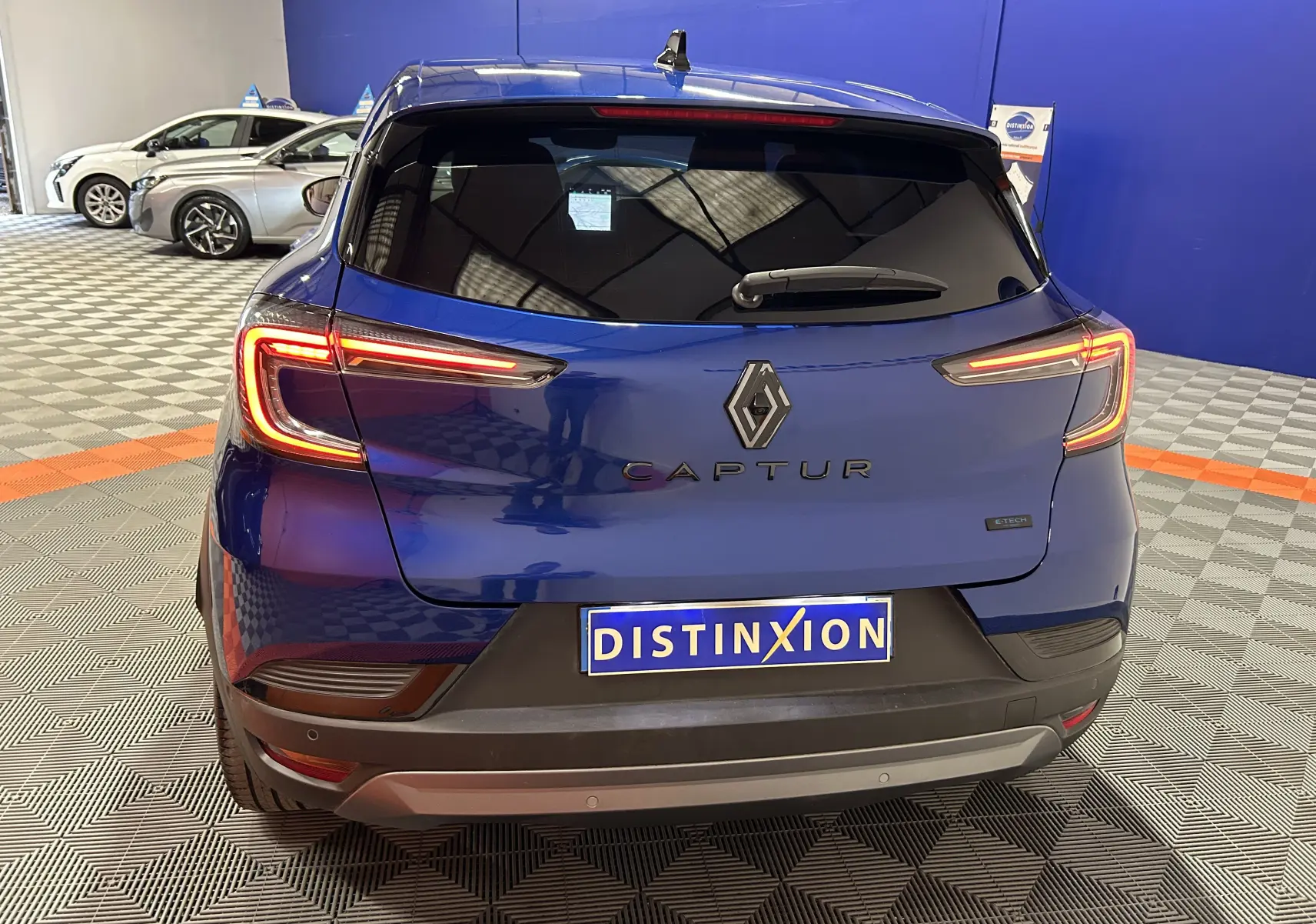 Vue arrière d'un Renault Captur bleu Iron avec feux LED allumés dans un showroom intérieur.