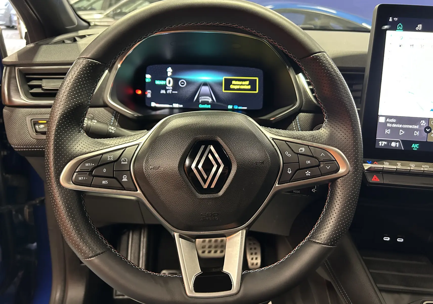 Vue rapprochée du volant noir perforé avec logo Renault, tableau de bord numérique et écran tactile du Renault Captur bleu Iron.