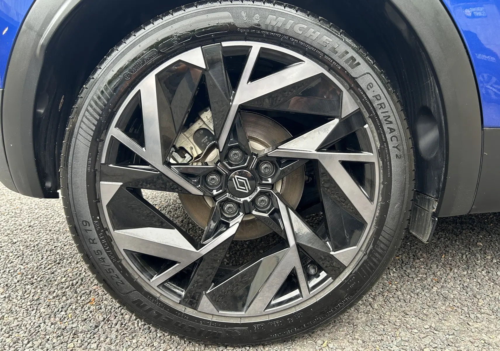 Gros plan sur la roue avant droite du Renault Captur bleu Iron, mettant en valeur la jante alliage noire et grise au design géométrique.